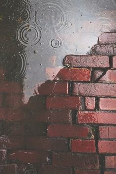 a red brick wall with water on it and raindrops in the sky above