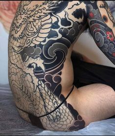 a man with dragon tattoos on his body and chest is sitting in the middle of a bed