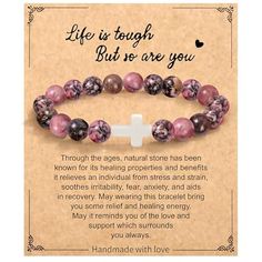 a bracelet with pink beads and a cross on the front saying life is tough but we are you