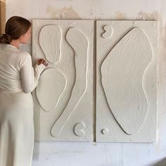 a woman standing in front of a white wall with two large pieces of art on it