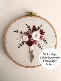 an embroidery pattern with white and red flowers on it, hanging from a wooden hoop