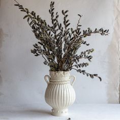 a white vase filled with plants on top of a table