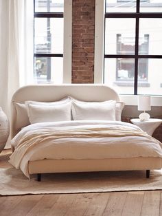 a bed with white linens and pillows in a bedroom next to a large window