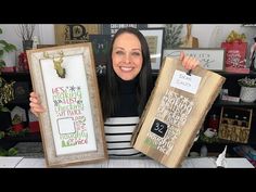 a woman holding up two framed pictures in front of a table full of christmas decorations