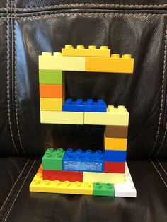 the letter e is made out of legos and sits on a black leather couch