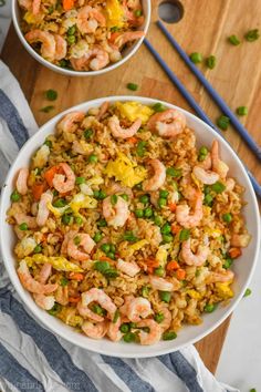 two bowls filled with shrimp and rice on top of a wooden table next to chopsticks