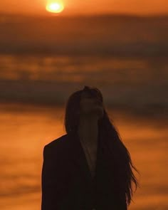 a woman standing on the beach at sunset looking up into the sky with her eyes closed