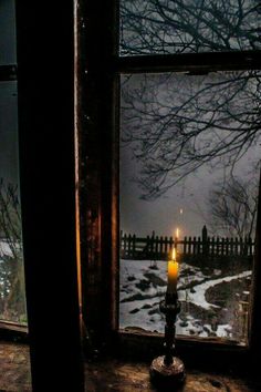 a candle is lit in front of an open window with snow on the ground and trees outside