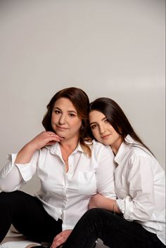 two women are sitting on the floor posing for a photo with their arms around each other