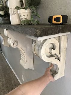 a hand is pointing at an old shelf with flowers and other items on top of it