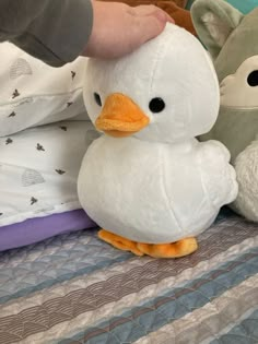 two stuffed animals sitting on top of a bed next to a person's hand