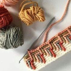 three balls of yarn and two skeins of knitting needles on a white surface