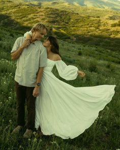 a man and woman are standing in the middle of a field with mountains behind them