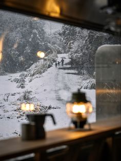 two people walking down a snow covered road in the middle of winter, through a window