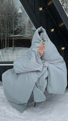 a woman wrapped up in a blanket and holding a glass of wine while standing on snow covered ground