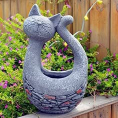 a cat statue sitting on top of a wooden fence next to flowers and plants in a garden