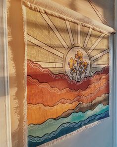 a wall hanging with flowers on it in front of a window and the sun shining through