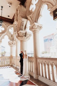 a bride and groom standing in the middle of an ornate building with columns on either side