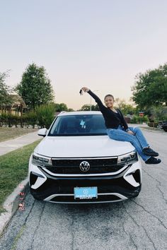 a woman sitting on the hood of a white car with her arms in the air