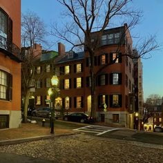 an empty street with cars parked on the side and buildings in the background at dusk