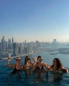 three women in the water holding up wine glasses with cityscape in the background