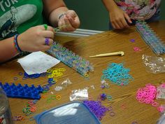 two girls are making bracelets with plastic beads and scissors on a wooden table in front of them