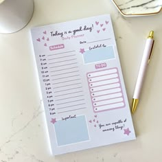 a pink and blue planner next to a pen on top of a white countertop