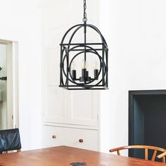 a chandelier hanging over a wooden table in a white dining room with black leather chairs