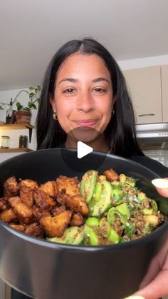 a woman holding up a bowl full of food