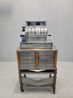 an old fashioned machine sitting on top of a metal table next to a white wall