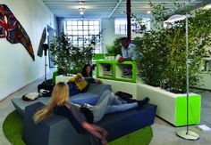 two people sitting on couches in an office with green plants and potted trees