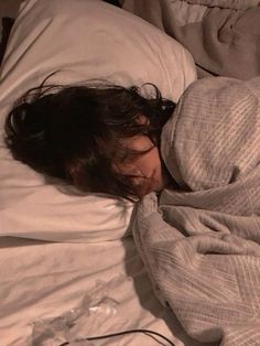 a woman sleeping in bed with her head on the pillow and eyes closed, covered by an overstuffed blanket