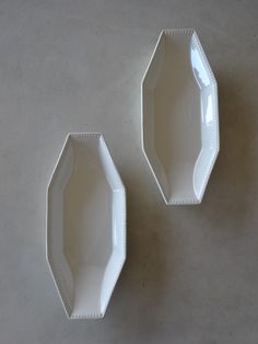 two white hexagonal dishes sitting next to each other on a gray surface,