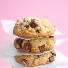 three chocolate chip cookies stacked on top of each other in front of a pink background