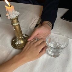 two people holding hands at a table with a candle in the middle and an empty glass next to them