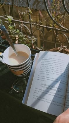 an open book sitting on top of a table next to a coffee cup and spoon