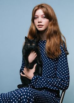 a woman with red hair holding a black cat in her lap and sitting on a chair