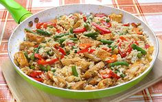 a pan filled with rice and vegetables on top of a wooden cutting board next to a green spatula