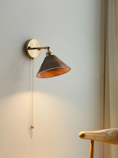 a wall mounted lamp on the side of a white wall next to a wooden chair