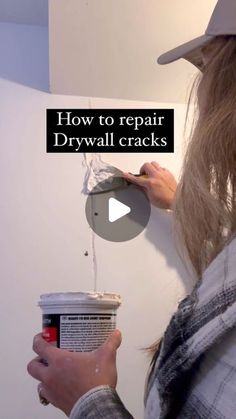 a woman is painting the wall with white paint and she is holding a can of drywall cracks