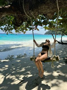 a woman is sitting on a swing by the beach