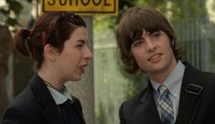 two people standing next to each other in front of a school sign and street sign