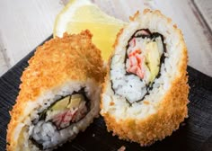 two pieces of sushi on a black plate with a lemon wedge next to it