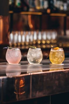 three different colored drinks sitting on top of a bar