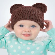 a baby wearing a brown bear hat with polka dots on it's shirt and blue eyes