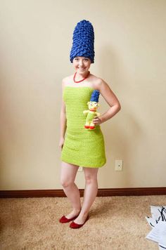 a woman in a green dress and blue knitted hat is holding a small toy