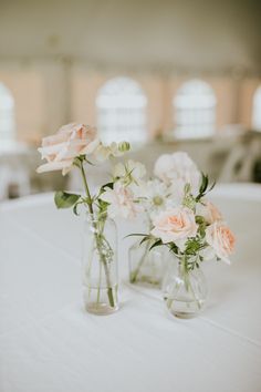 two vases with flowers are sitting on a white table cloth covered round tablecloth