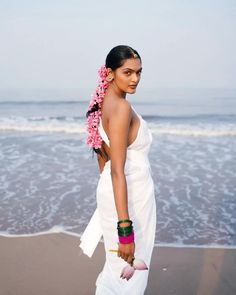 a woman in a white dress on the beach with flowers in her hair and bracelets around her neck