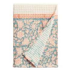 an orange and blue floral print blanket on top of a white tablecloth with two folded napkins