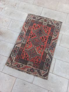 a red and black rug on the ground in front of a white tiled flooring